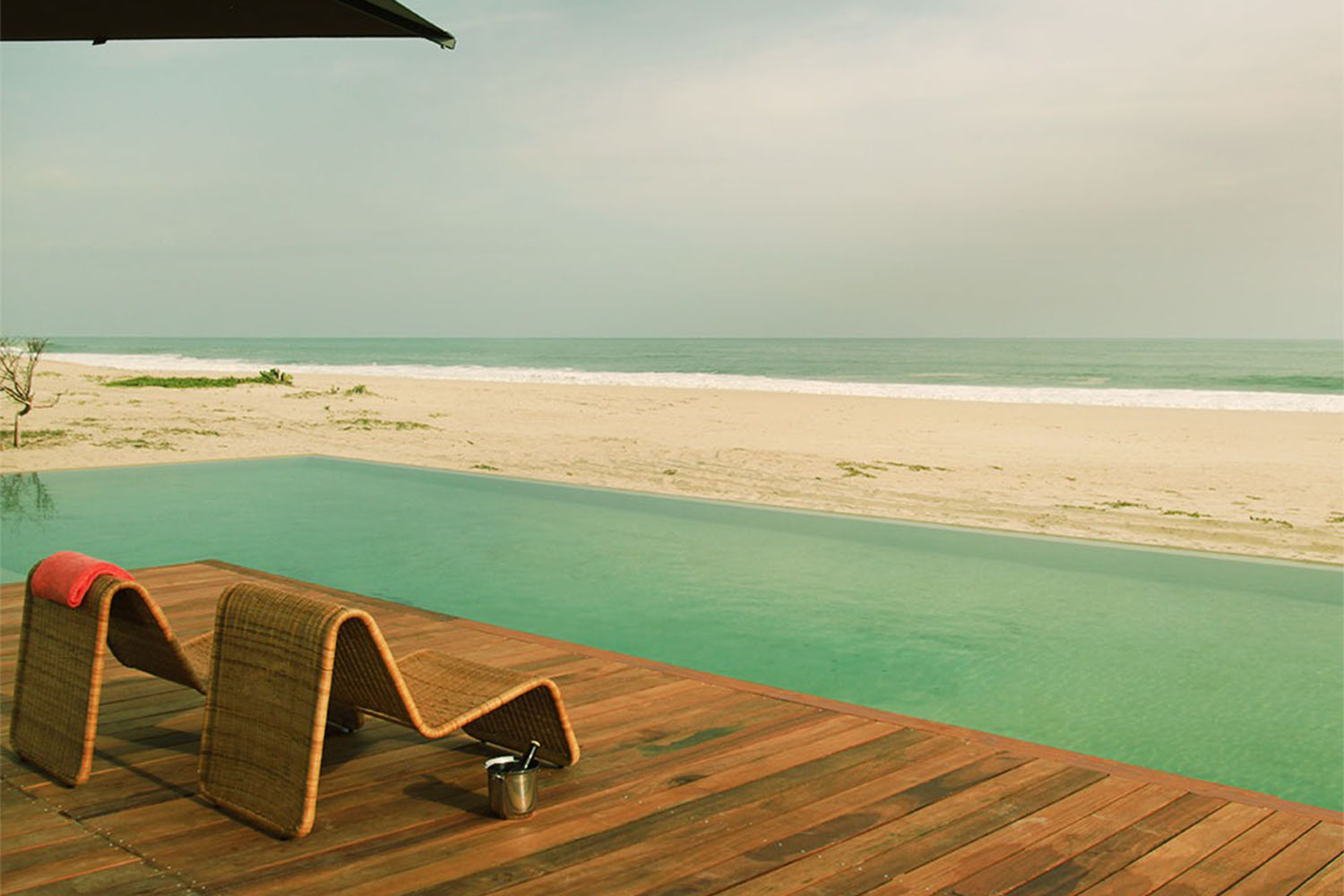 Two lounge chairs on the deck of a sand-bottom pool, facing the ocean