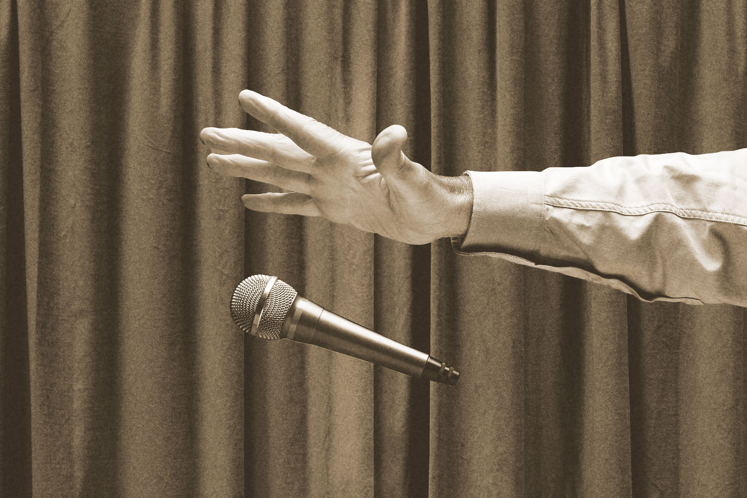 A gloved hand drops a microphone in front of a curtain.