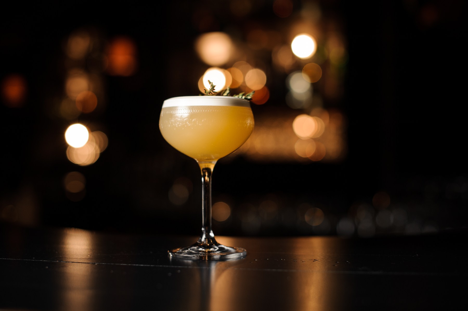 Light brown cocktail with smoldering rosemary branch on a bar counter
