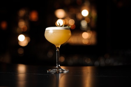 Light brown cocktail with smoldering rosemary branch on a bar counter