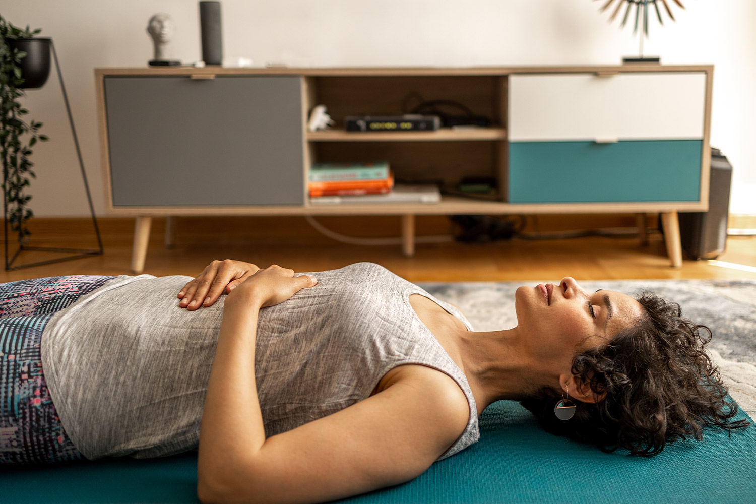 Woman taking a deep breath lying on exercise mat in apartment