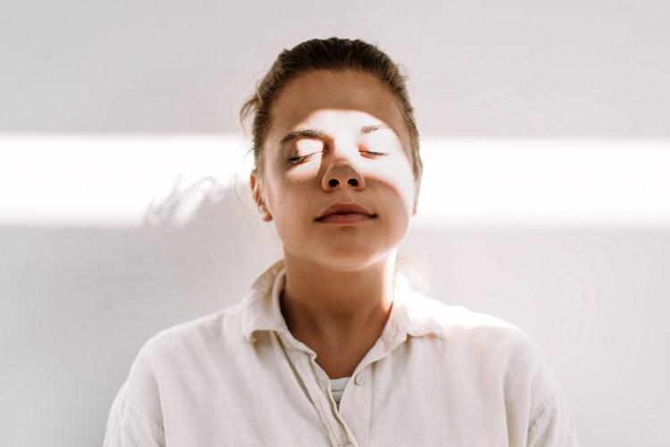 Woman practicing deep breathing in front of beige wall