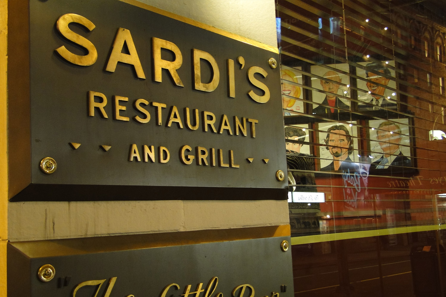 Outdoor sign to Sardi's Restaurant and Grill and caricatures on the wall seen through the window