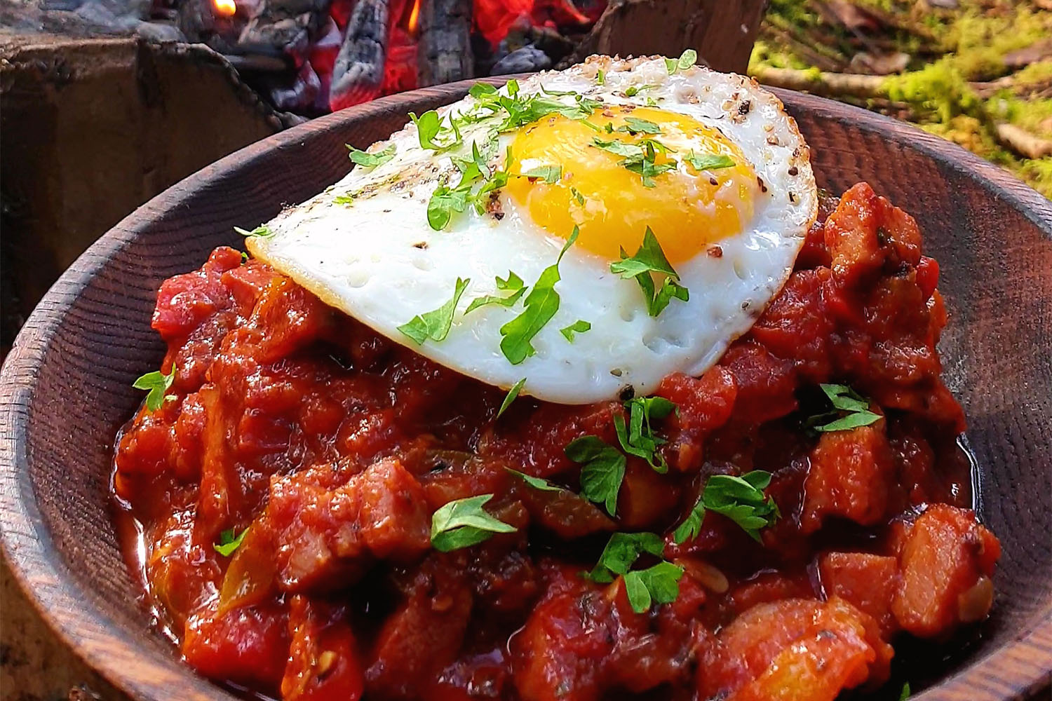 A bowl of cooked meat with an egg on top in a bowl outside.