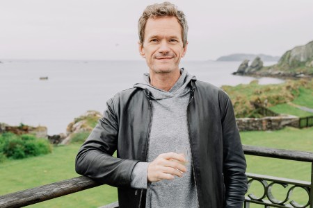 Neil Patrick Harris standing on a terrace with a glass in his hand.