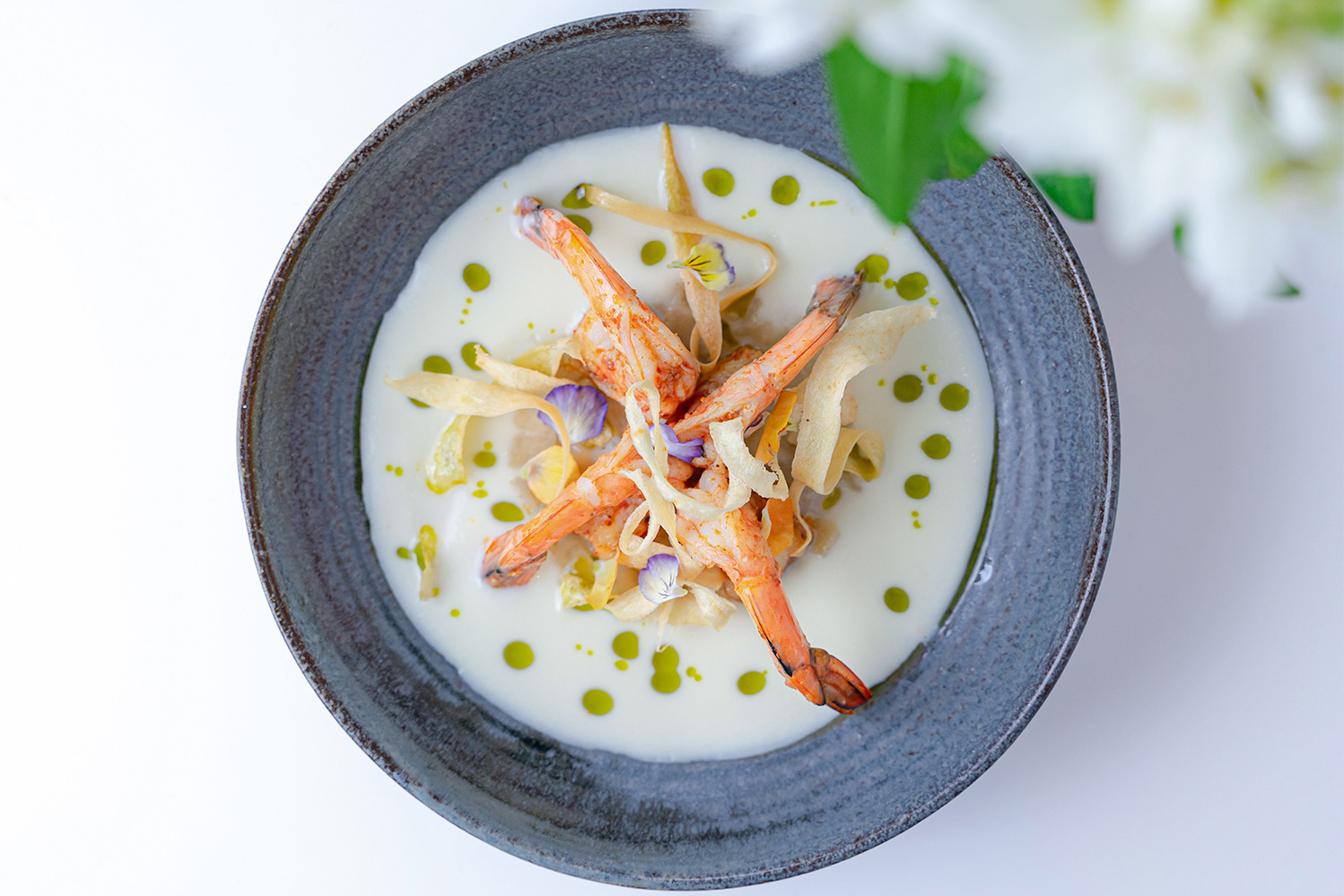 Gourmet presentation of apple and parsnip soup shown from above with shrimp and a purple flower garnish