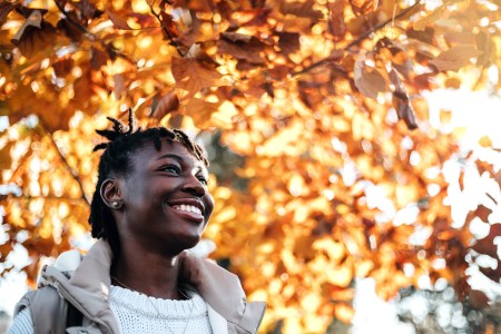 Woman in sweater and vest smiling with orange autumn leaves behind her