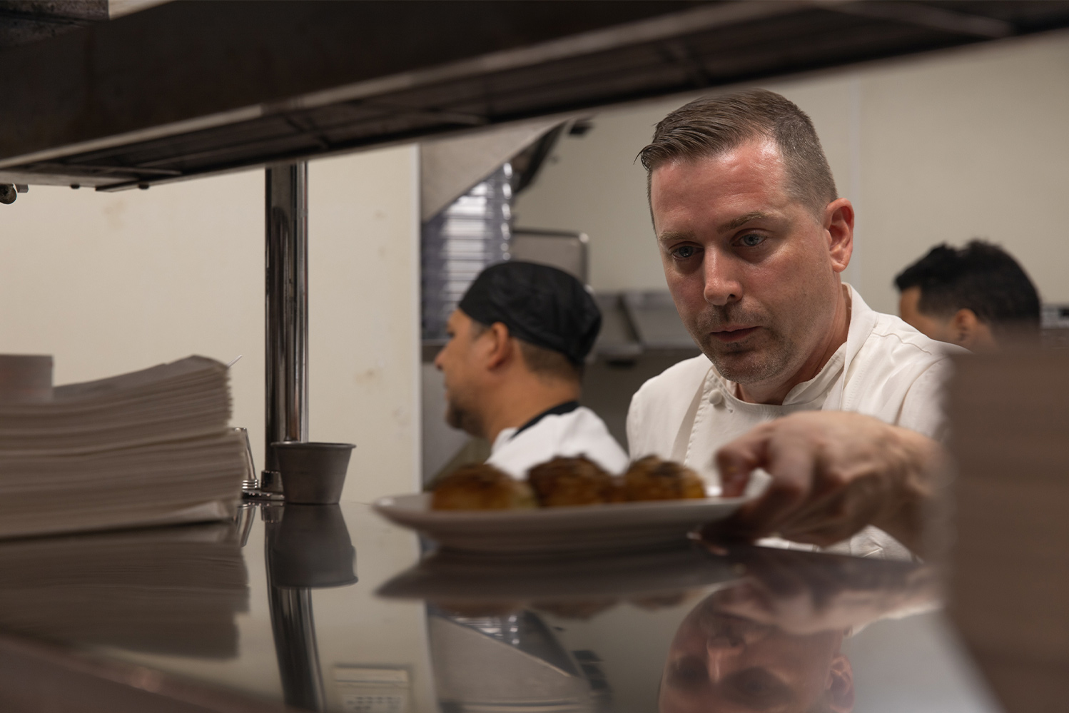 Chef Ed Cotton setting a dish of food from the kitchen cooking line to the expo counter under heating lamps