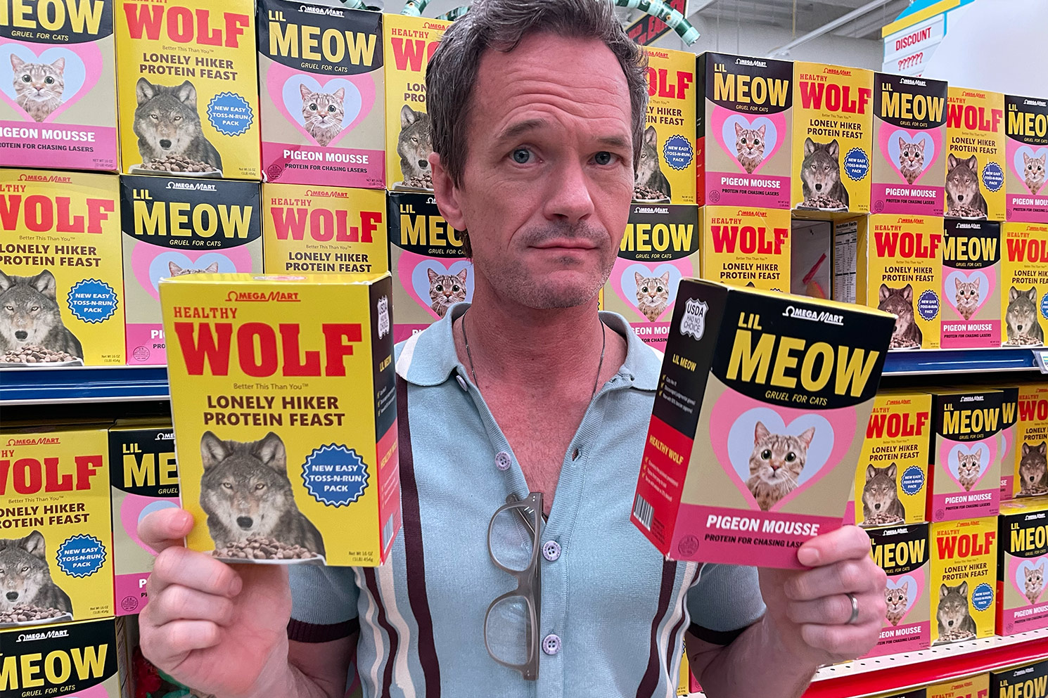 Neil holding two boxes of feating "gifts" for cats and wolves in from of wall full of featured gift