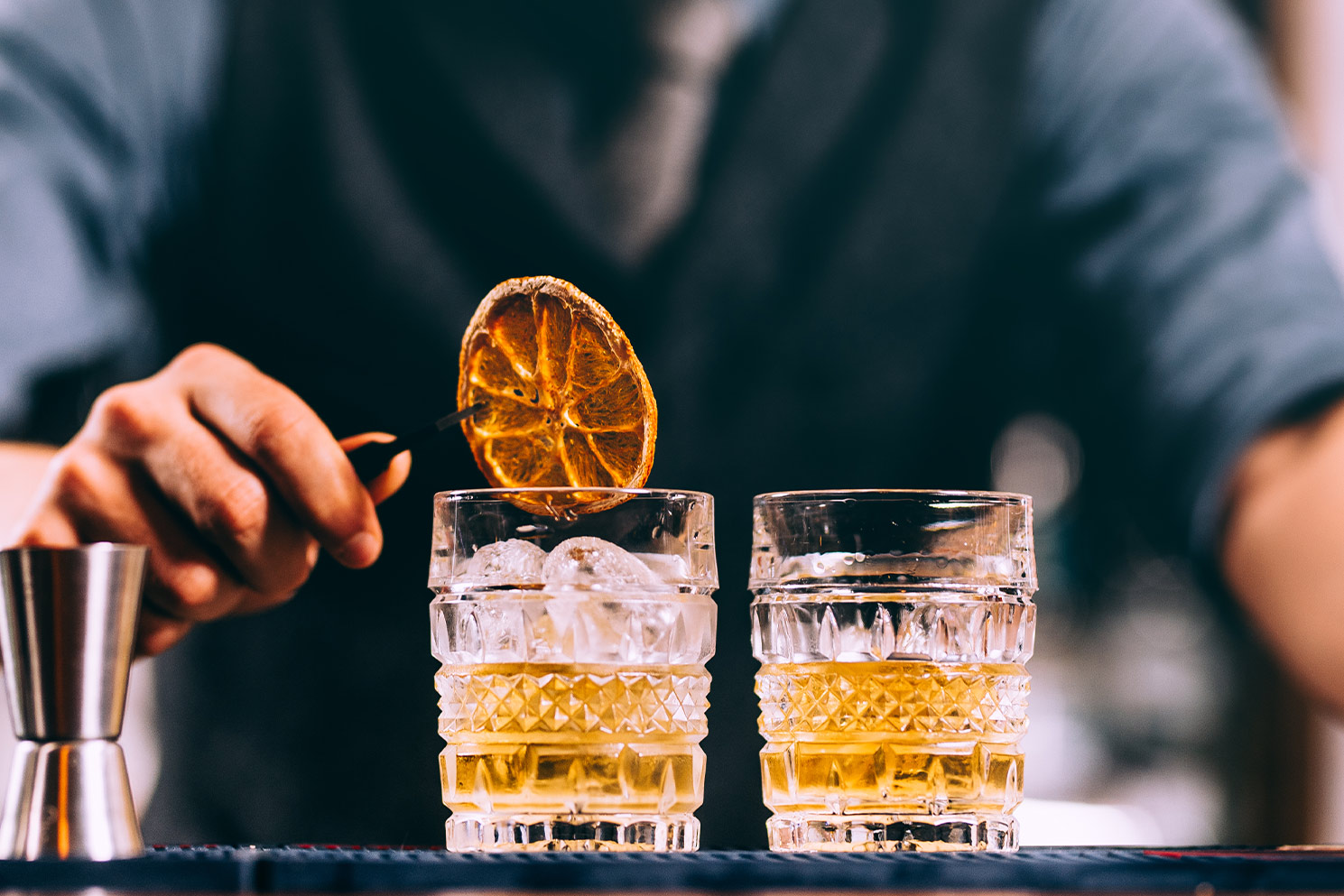 A bartender placing a dried orange wheel on top of two tequila drinks in glasses