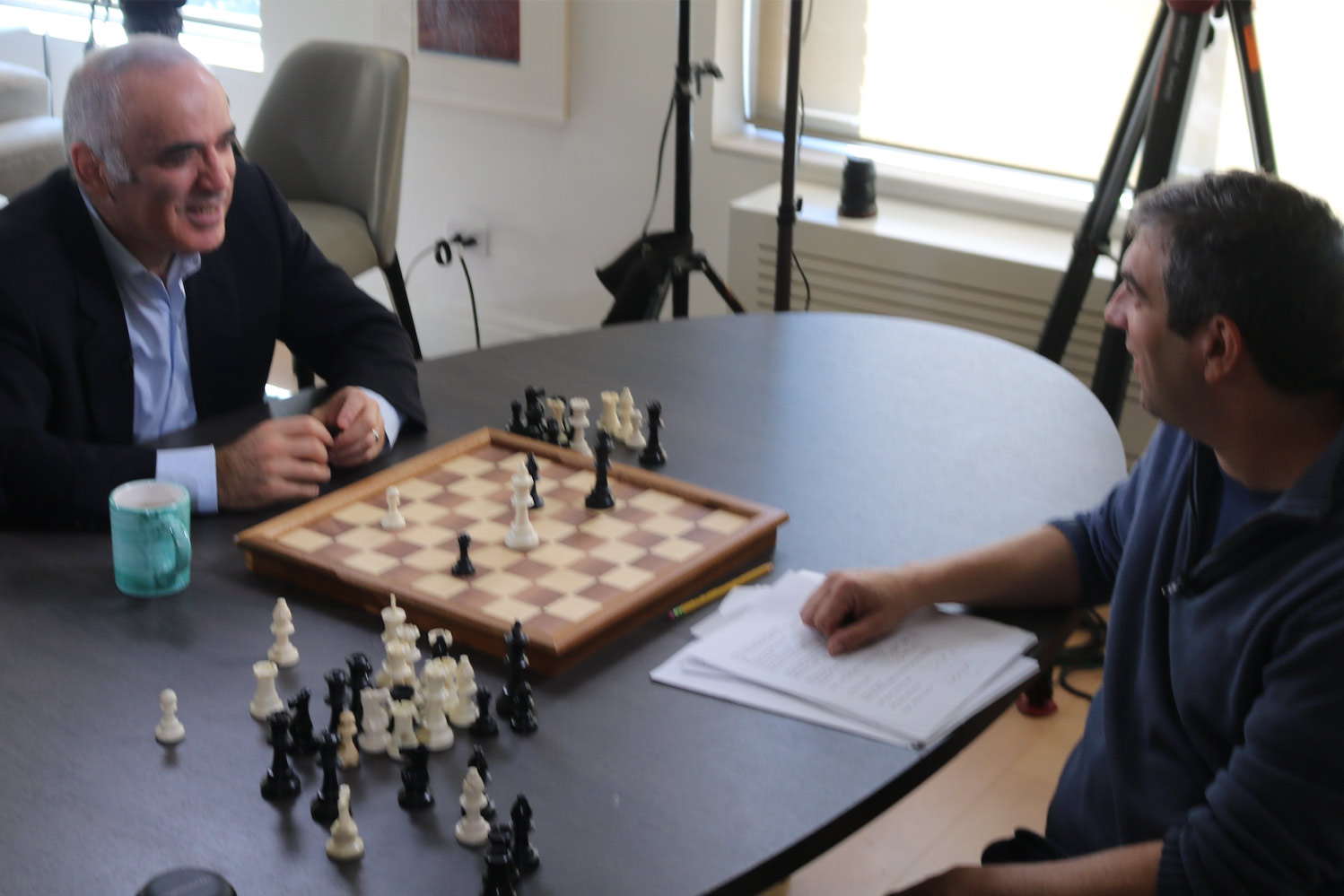 Podcast host A.J. playing chess on a round table across from Garry Kasparov