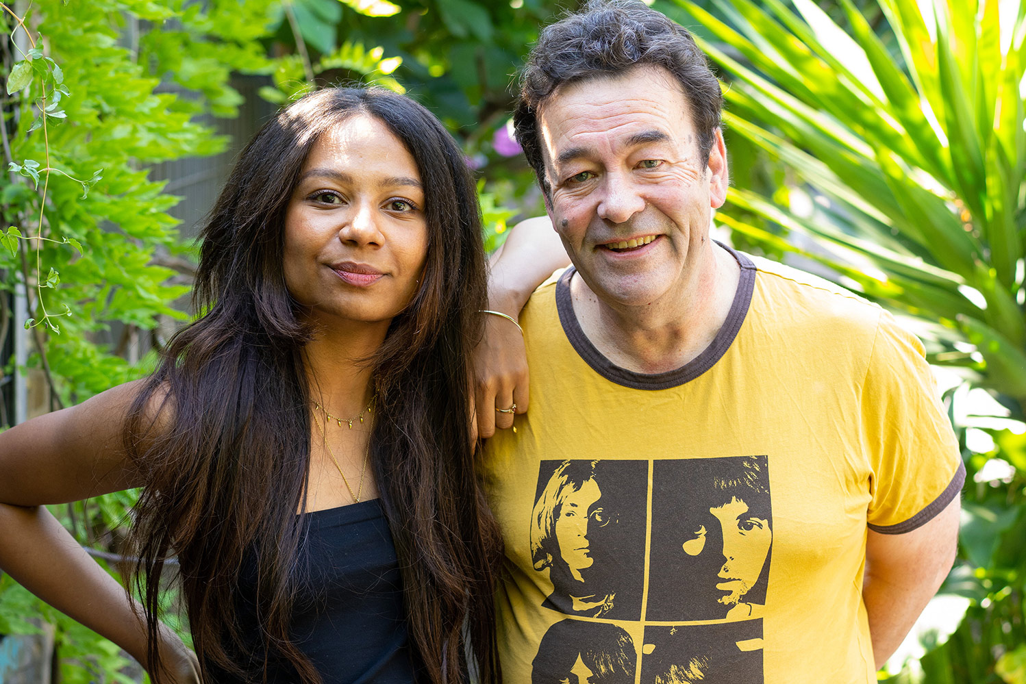 Jo Hamya poses with arm over James Walton shoulder in front of palms and greenery