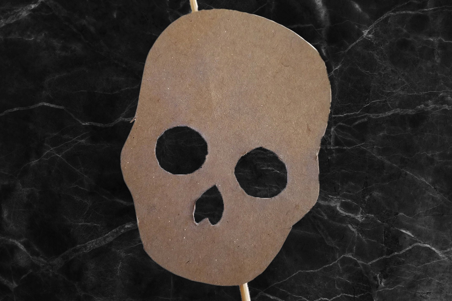 A cardboard cut-out of a skull taped to a stick on a black marble background