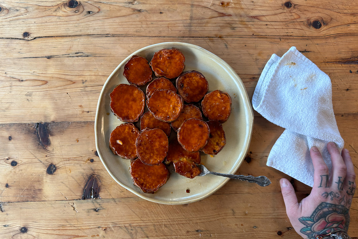 Plate of sweet potatoes with a hand holding a towel on a wood butcher table
