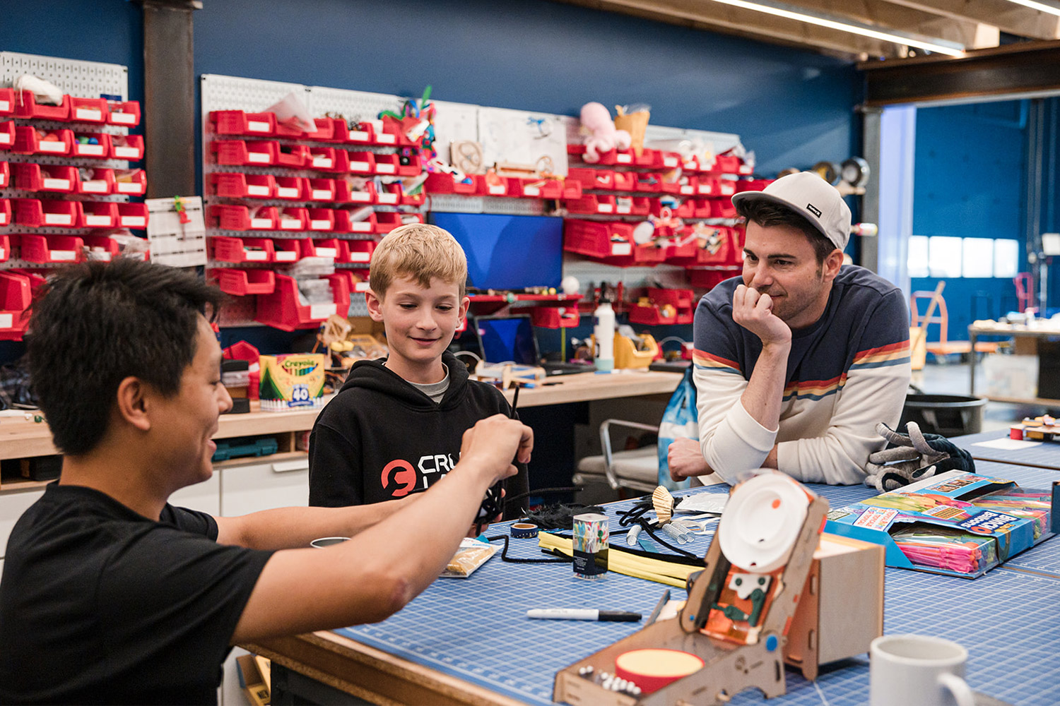 Two adults and a child in a workshop tinkering with tools and supplies