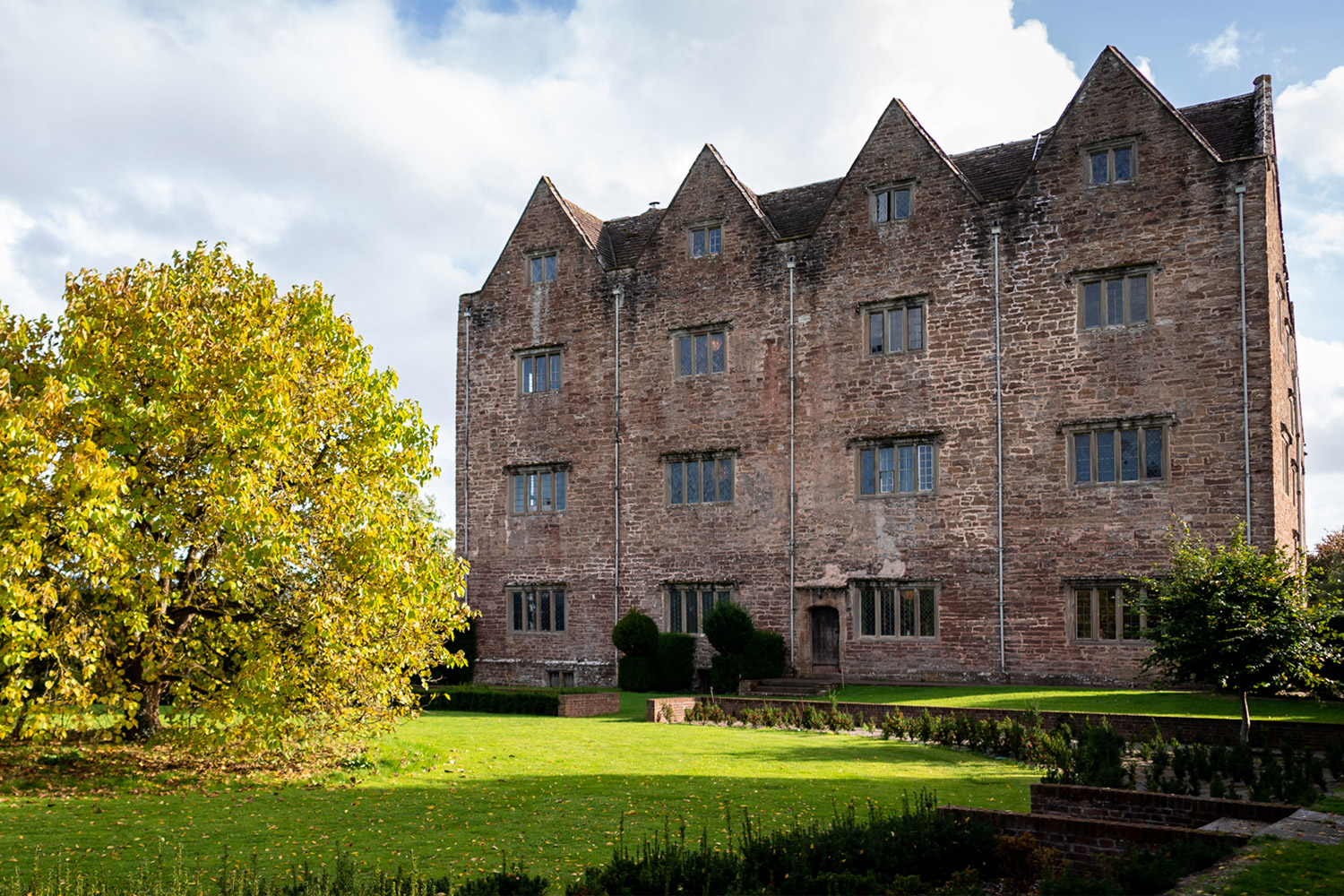 The front view of an old brick Welsh manor from the 1600s with green grass