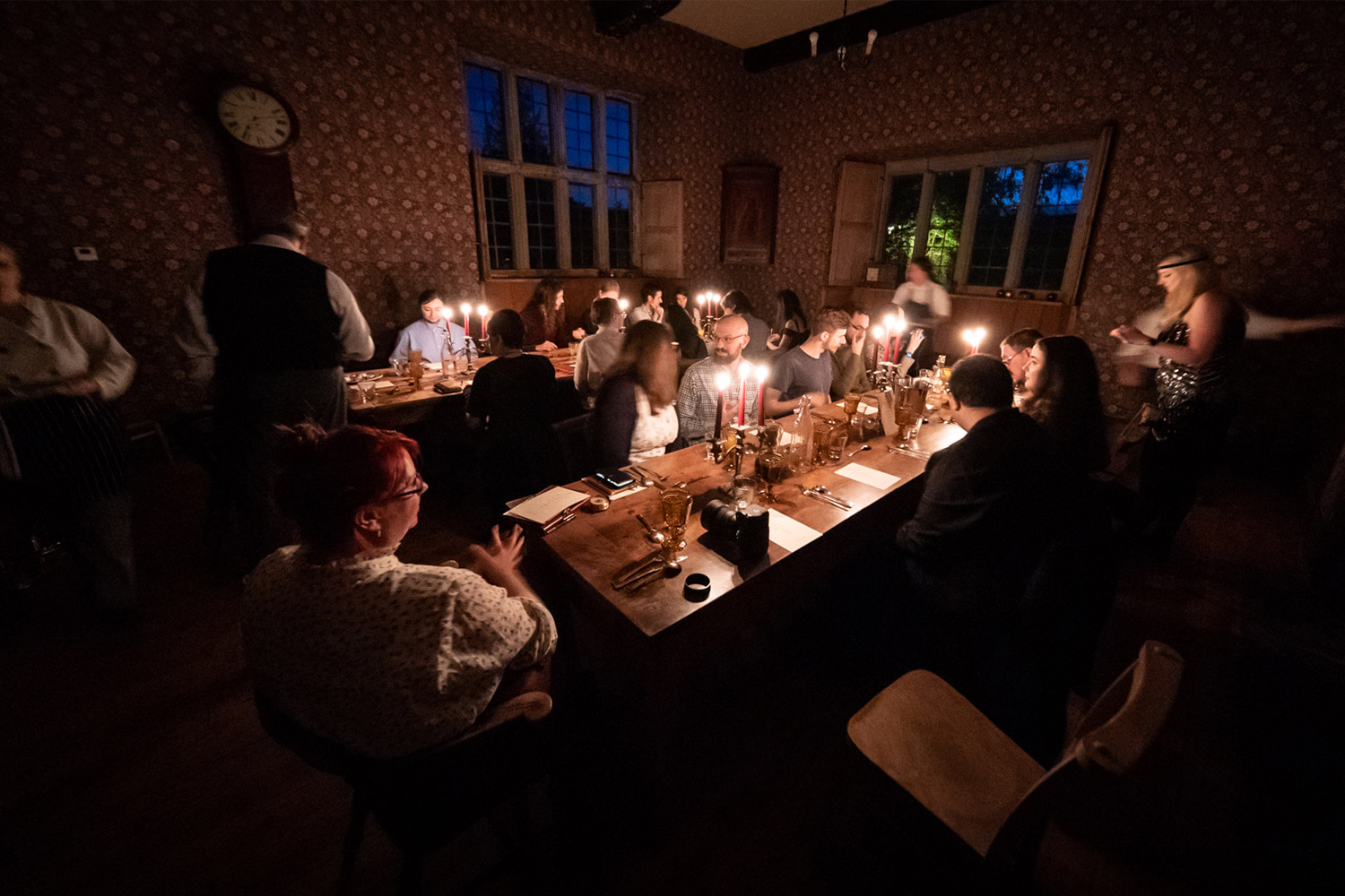 A wide view of two dinner tables full of people by candlelight