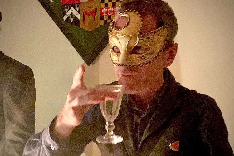 Neil Patrick Harris sips a drink wearing a gold mask by candlelight