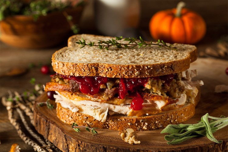 Turkey sandwich on wheat bread filled with stuffing and cranberries surrounded by rosemary and sage herbs