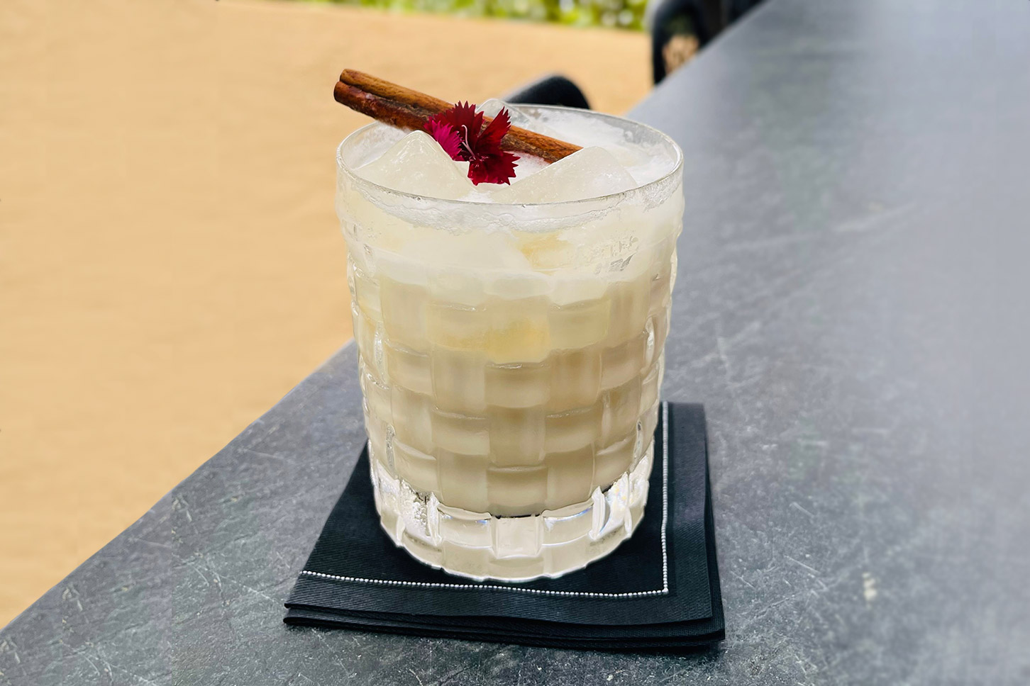 Tropical iced cocktail with cinnamon stick and pink flower on grey countertop
