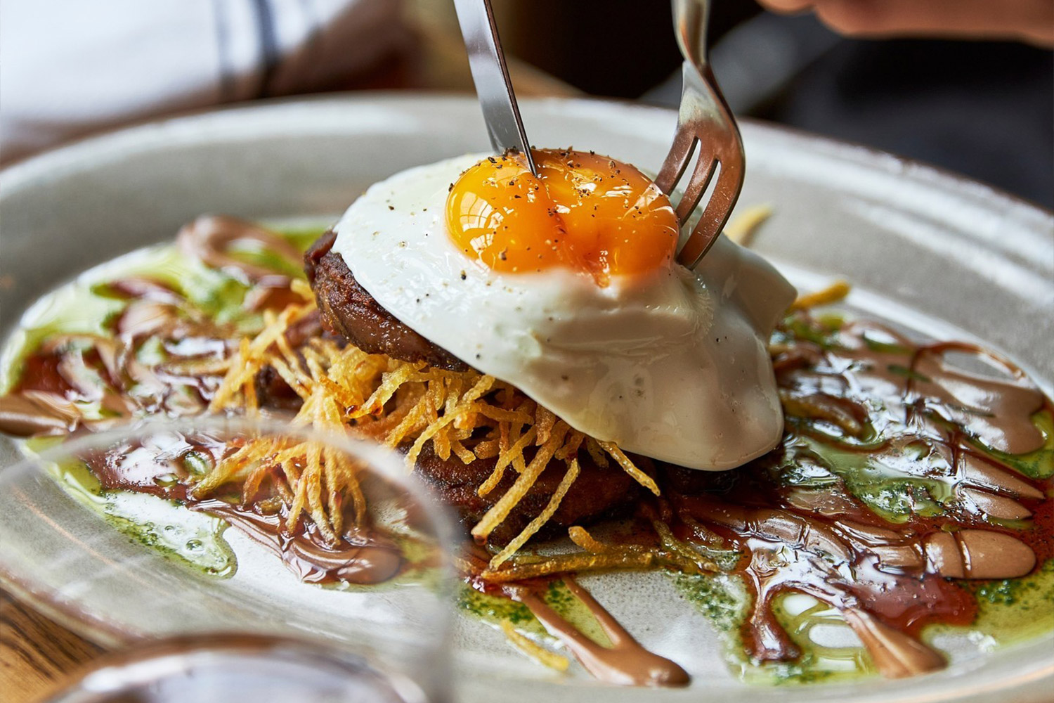 Brunch dish showing someone cutting into the yolk of an egg on top