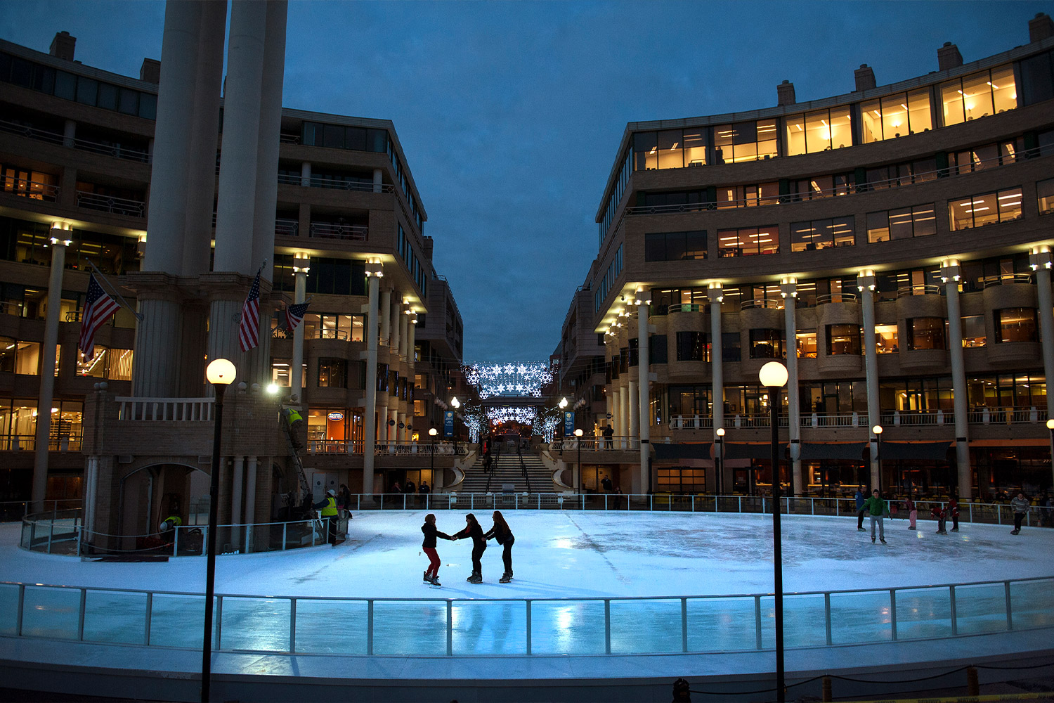 People skating on an ice rink between two buildings at night
