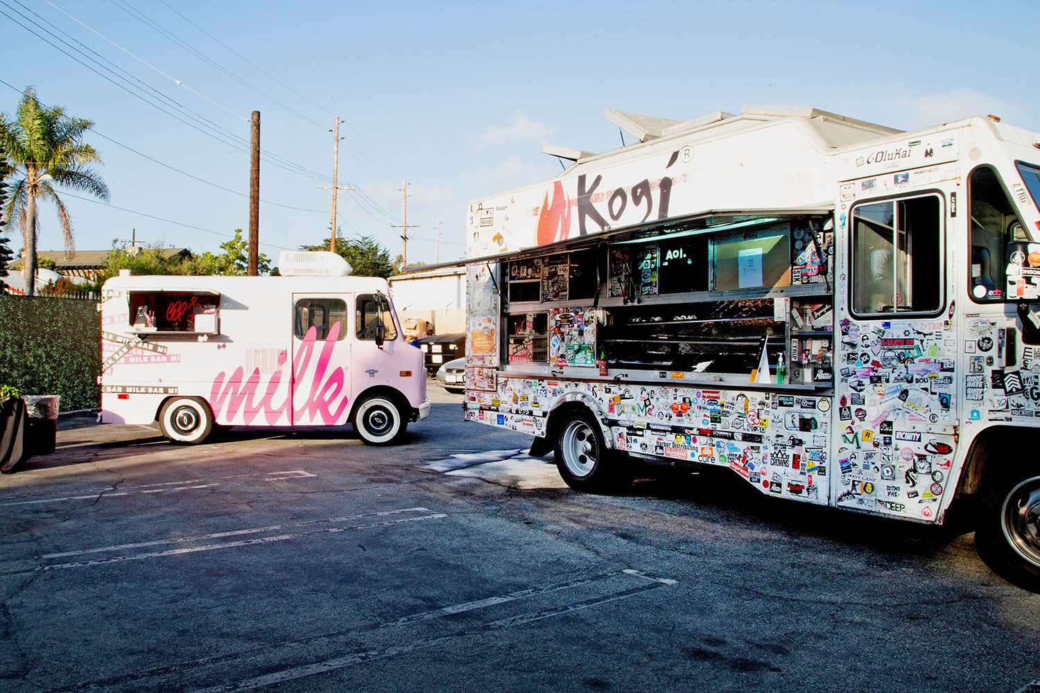 Two food trucks in a parking lot with palm trees in background