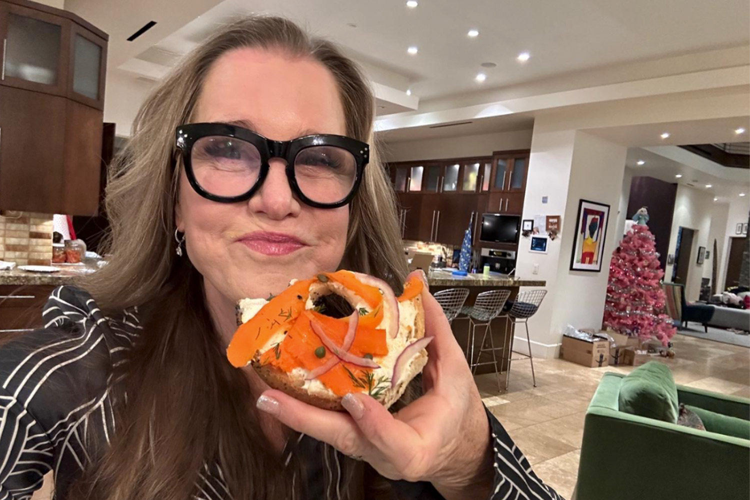 Woman in glasses holding a bagel and smiling