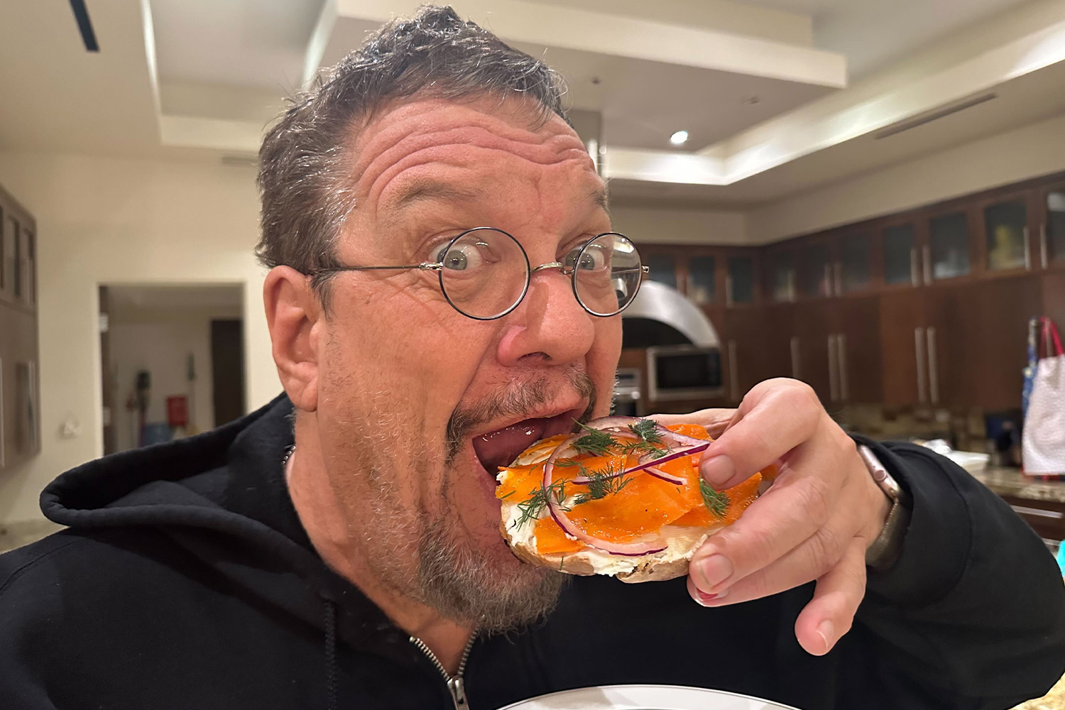 Man in glasses eating a bagel looking excited