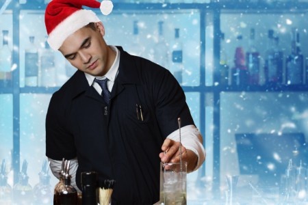 Bartender making a drink wearing a santa hat with fake snow all around