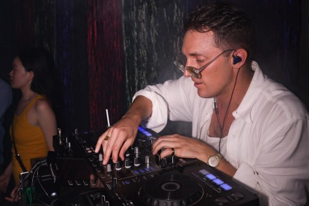 A DJ wearing sunglasses and adjusting his turn table