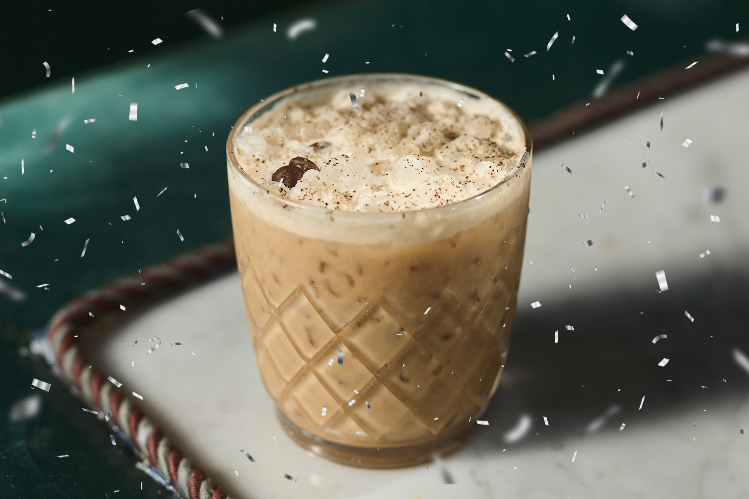An iced coffee cocktail in a rocks glass with silver confetti falling