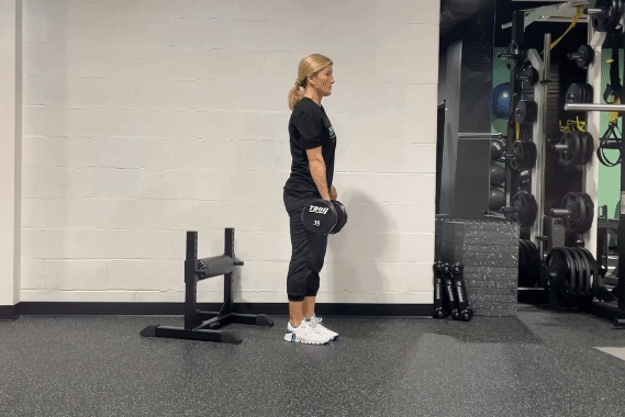Woman in a gym elevating her foot and lunging backward with weights in her hand