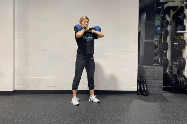Woman squatting in a gym with kettlebells on her shoulders