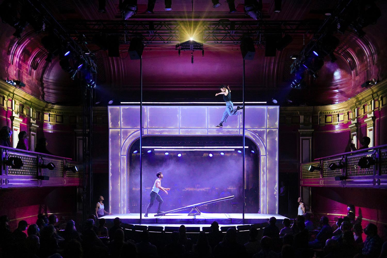 Two men on stage with one suspended into the air launched from a seesaw