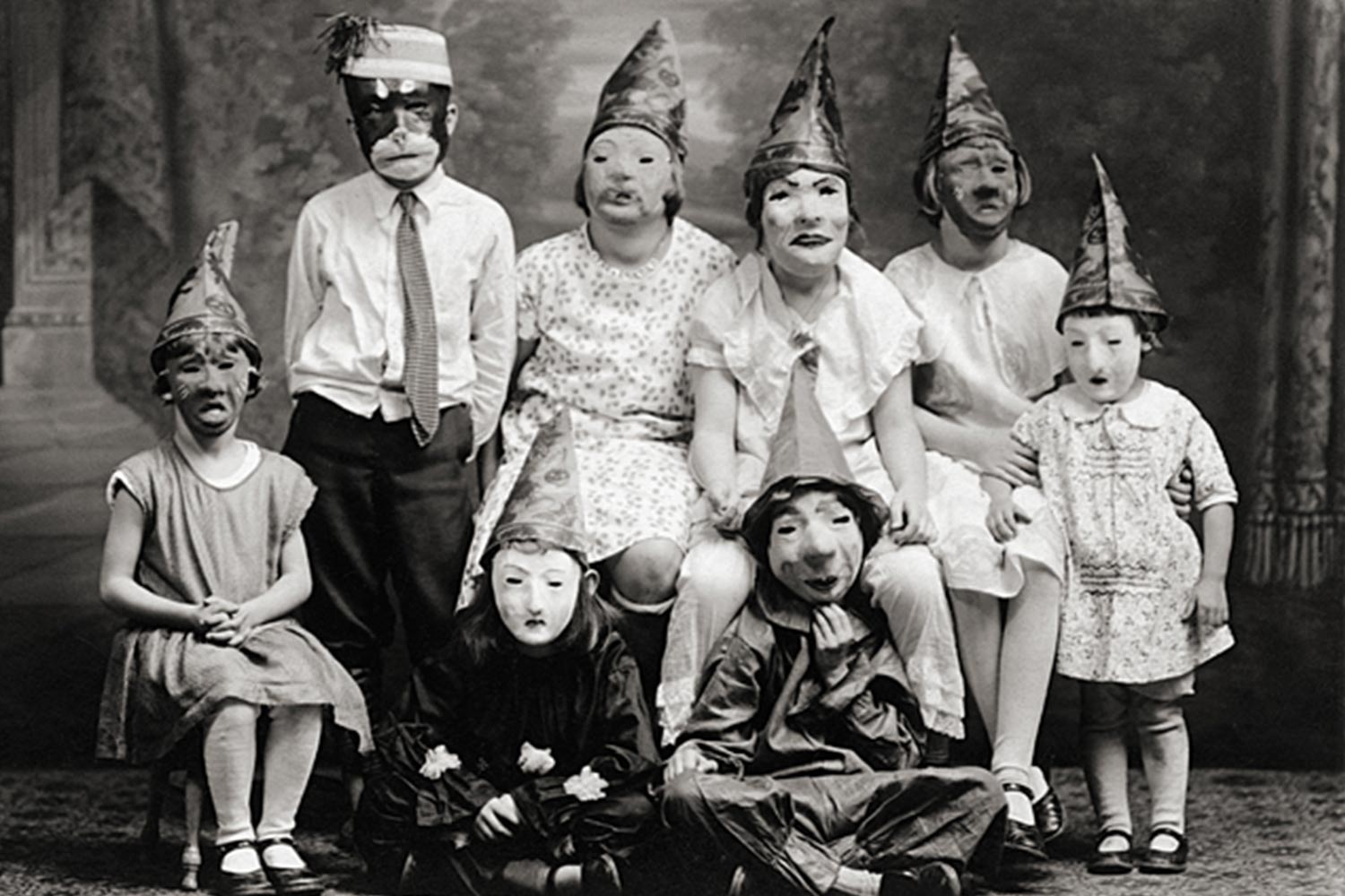 B&W photograph of a group of children wearing masks and pointed hats