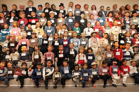Nearly one hundred ventriloquist dolls posed sitting in rows
