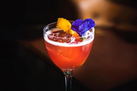 Red cocktail with flowers in a nick and nora glass